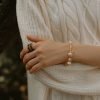 Trochus Shell Bracelet with Lotus | Wisdom & Wealth - Flow Collection Model with crossed arms wearing the Trochus Shell Bracelet with Lotus from the Flow Collection, showcasing lustrous cream beads for wisdom and wealth against a soft white cable-knit sweater.