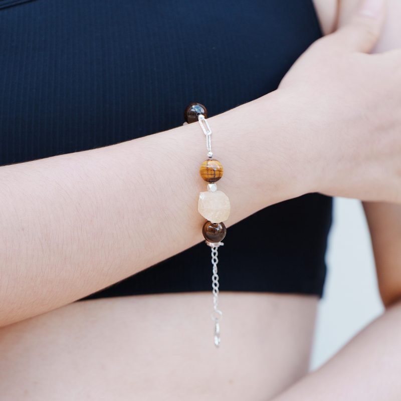 Model wearing the Citrine & Tiger's Eye Bracelet with Hexagram Charm from the Elementa Collection, featuring yellow and brown gemstone beads for confidence against a black top.