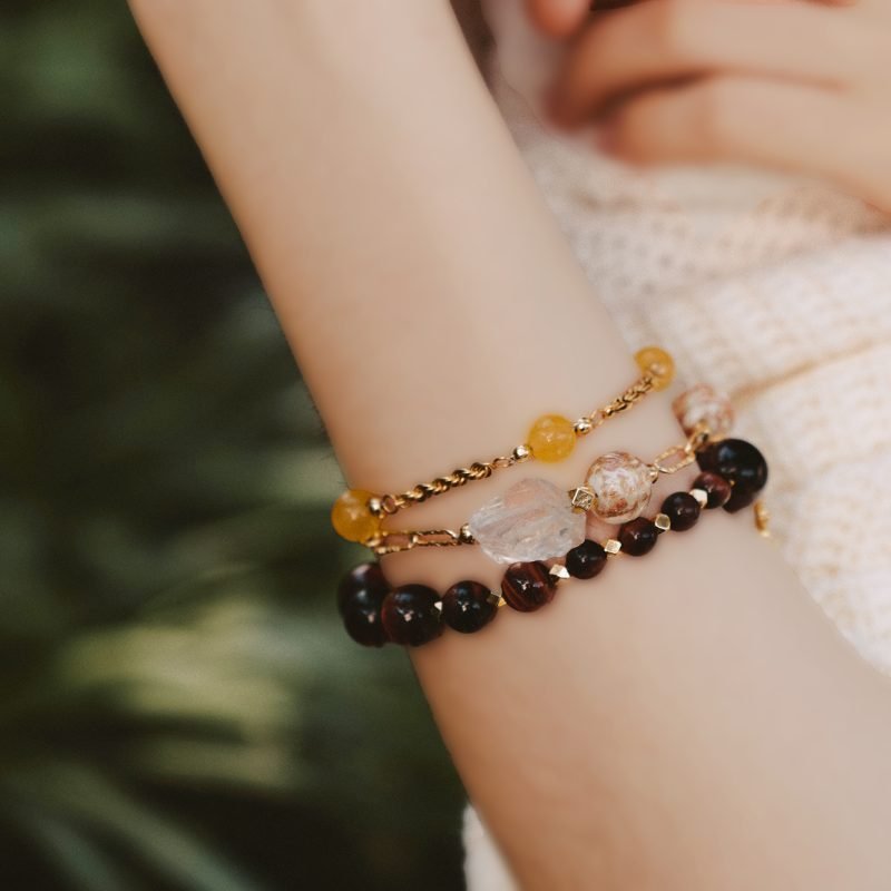 Model wearing the Yellow Jade Bracelet with Hexagram from the Vine Collection, stacked with other crystal bracelets for prosperity against a white knit top.
