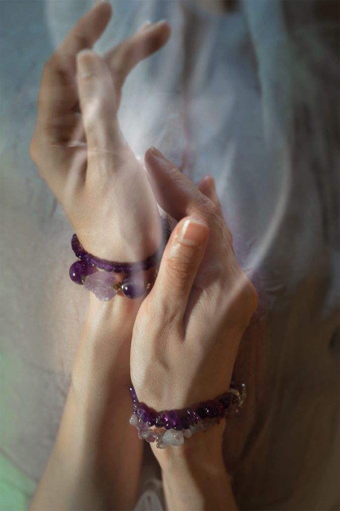 Close-up of hands wearing stacked raw Amethyst crystal bracelets for Crown Chakra spiritual connection and inner peace.